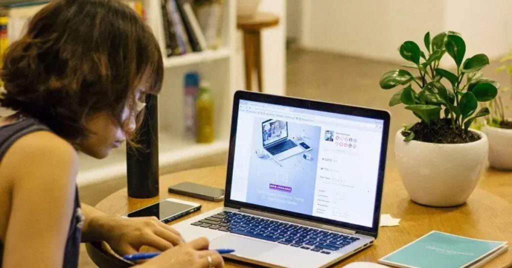 a woman sitting at a table using a laptop with product keys from Cheap Key Shop